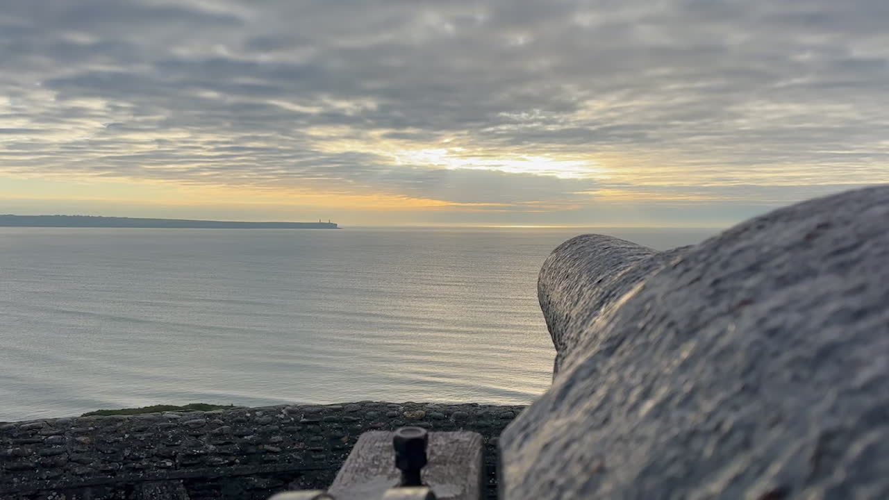 Dawn perspective view down barrel of old iron cannon overlooking ocean