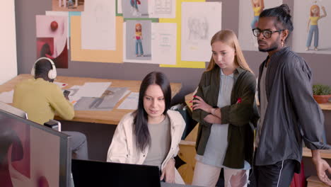 joven diseñadora gráfica explicando el proyecto en computadora a sus colegas multiétnicos en un estudio de animación 1
