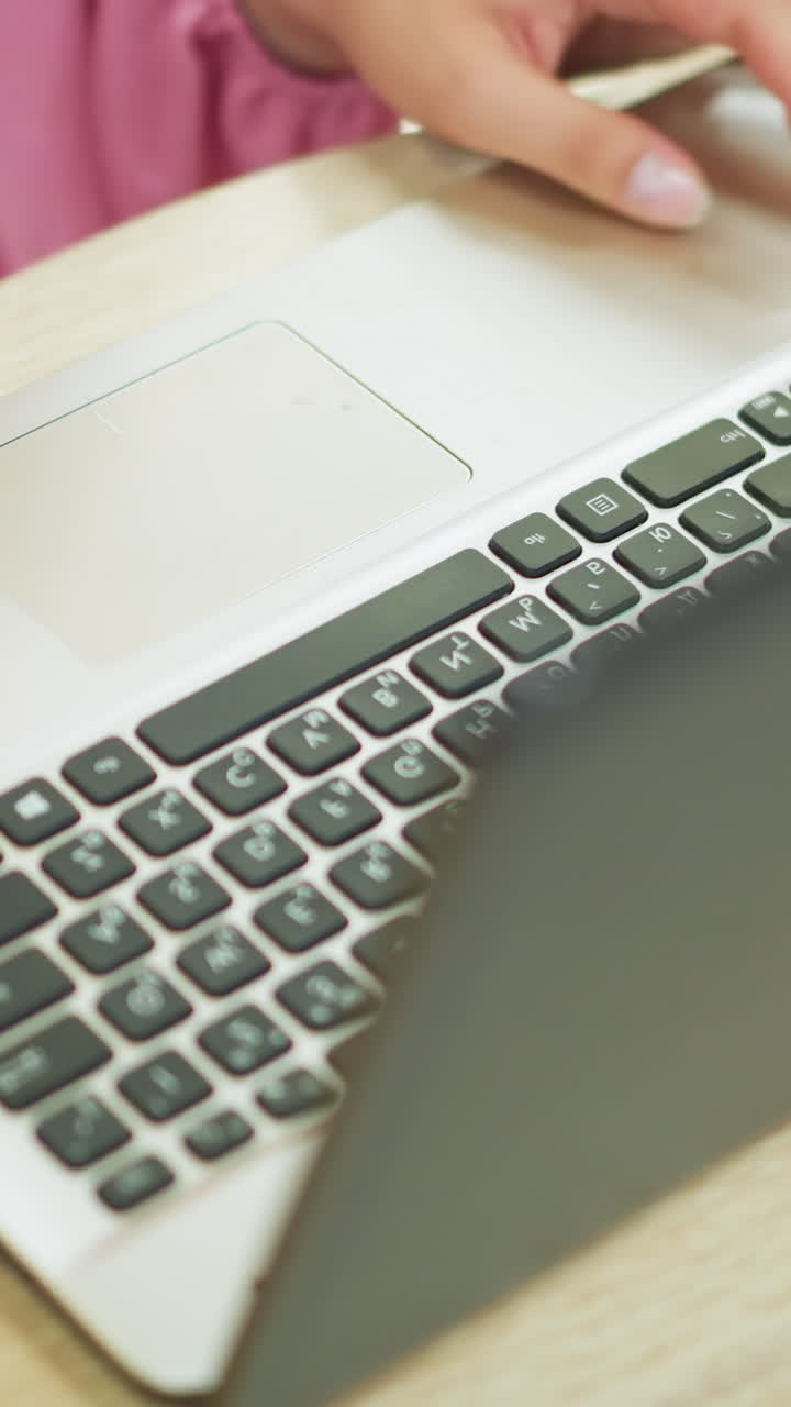 vista de la mano de una dama con un vestido rosa y una cadena de muñeca abriendo una computadora portátil en una mesa de madera, con la sombra visible en el teclado, preparándose para escribir, a medida que se abre la pantalla de la laptop, con el lugar bien iluminado