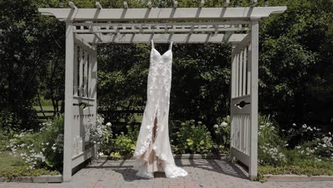 acercándose a un hermoso vestido de novia de diseñador colgando de una pérgola al aire libre durante un hermoso día en el centro de bodas y eventos strathmere en ottawa, canadá