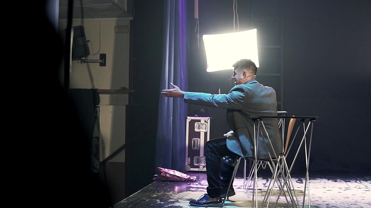 Magician sitting on a stage doing magic tricks. Shot in slow motion
