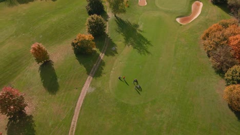 golfer beats the ball on the green during a beautiful sunny day in autumn - aerial drone static shot