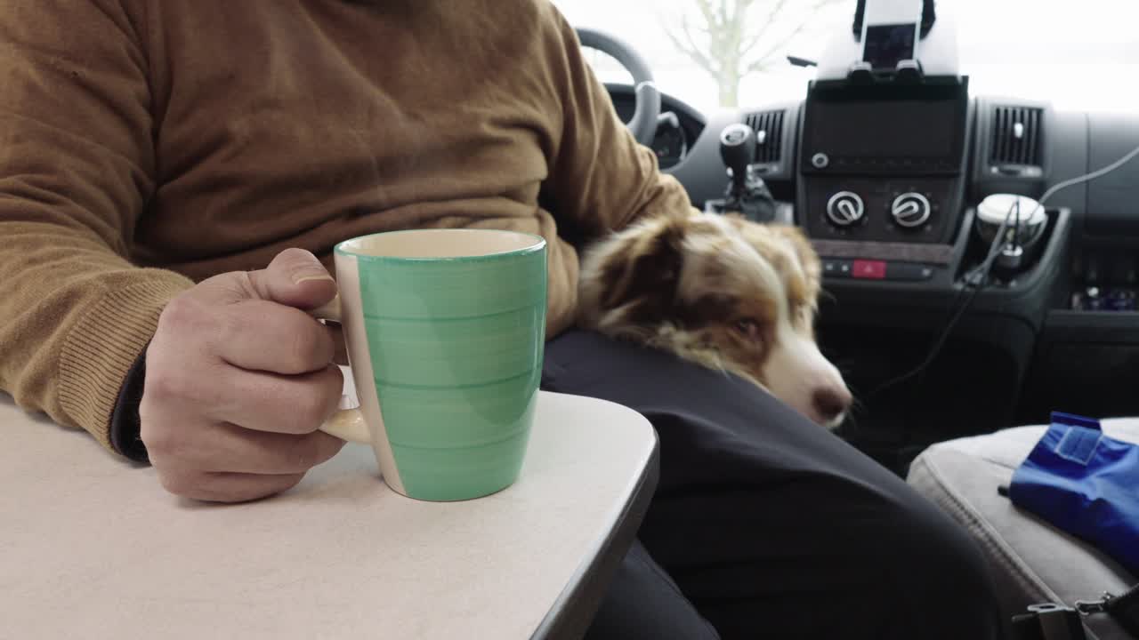 hombre mayor acariciando perro en autocaravana, taza de té o café en la mesa, vista interior