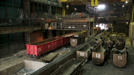 industrial interior of a steel mill with red cargo trains and numbered containers