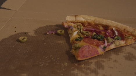 mano agarrando una rebanada de pizza de pepperoni con aceitunas y cebollas encima