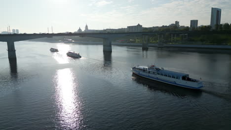 boats navigating a river under a bridge with city skyline