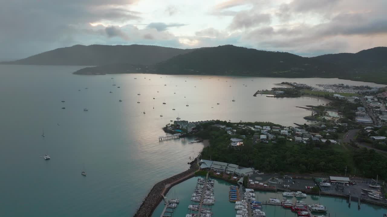 Port Airlie Beach Bay Lagoon Coral Sea marina aerial drone mist sunrise morning rain clouds heart of Great Barrier Reef Whitsundays Whitehaven jetty yachts sailboats circle right motion