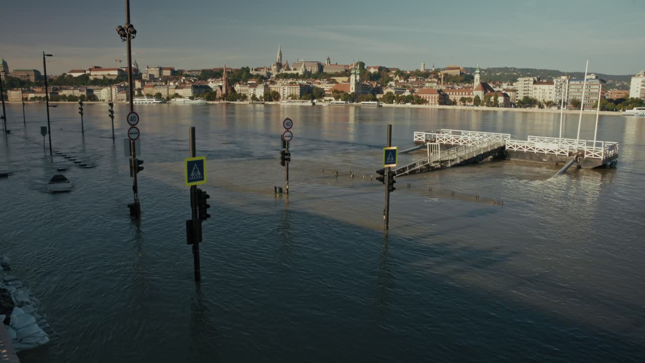 Flooded riverside with submerged traffic lights and signs, and a distant cityscape across the river, Budapest, Hungary