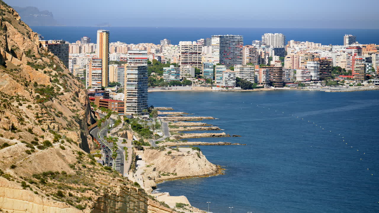 View of rocky promontories and breakwaters leading to a dense high rise waterfront in Alicante, Spain