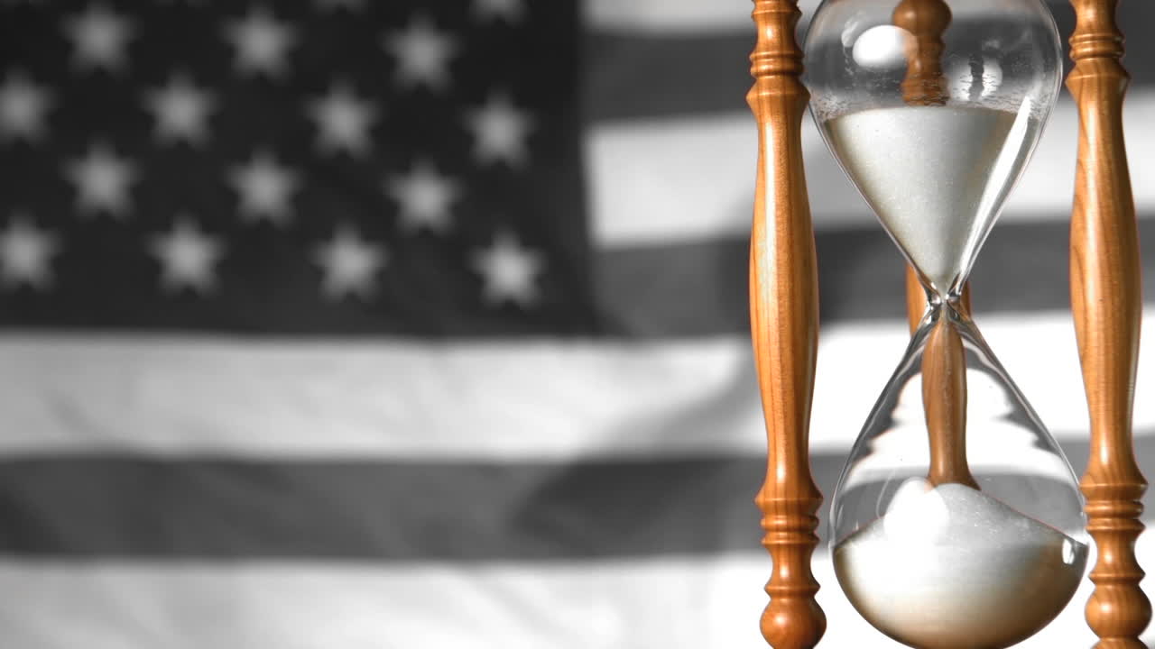 Sabbia che scorre attraverso una clessidra con la bandiera americana che sventola sullo sfondo