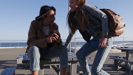 front view of a caucasian and a mixed race girl sitting on a table seaside