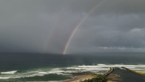 la desembocadura del río que conduce a una popular playa de surf con un arco iris deslumbrante y nubes de lluvia por encima de una ola turbulenta del océano