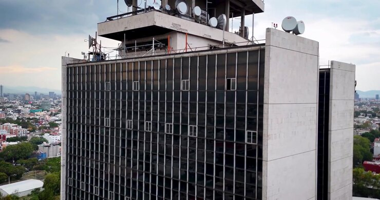 Vista da drone in avvicinamento a un grattacielo a Città del Messico, che rivela la sua facciata in vetro, le antenne sul tetto e l'ampio skyline metropolitano sullo sfondo