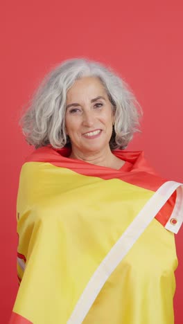 senior woman wrapped in a spanish flag on a red background