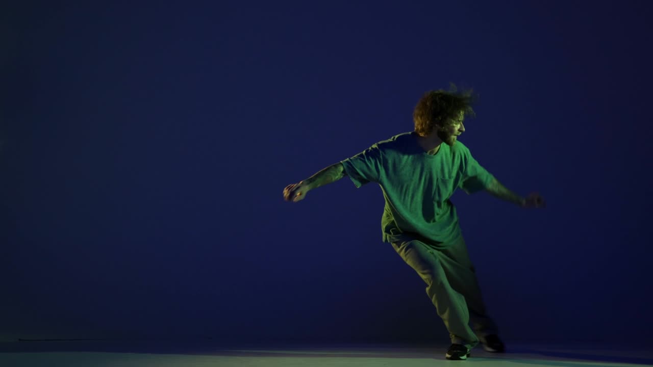 Stylish young man, hip-hop dancer dancing isolated over dark blue background in neon light. Modern dance art, fashion, youth, ad, style. 4K, video