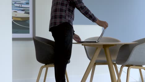 hombre asiático del reino unido caminando hacia la mesa llevando una computadora portátil e iniciando sesión en un espacio de trabajo remoto