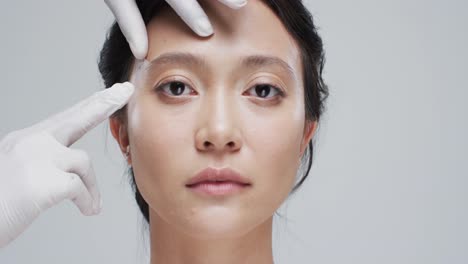 hands in gloves touching face of asian woman on grey background, slow motion