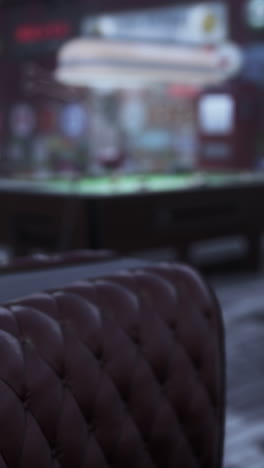a close-up of a red leather couch in a bar with a pool table in the background.