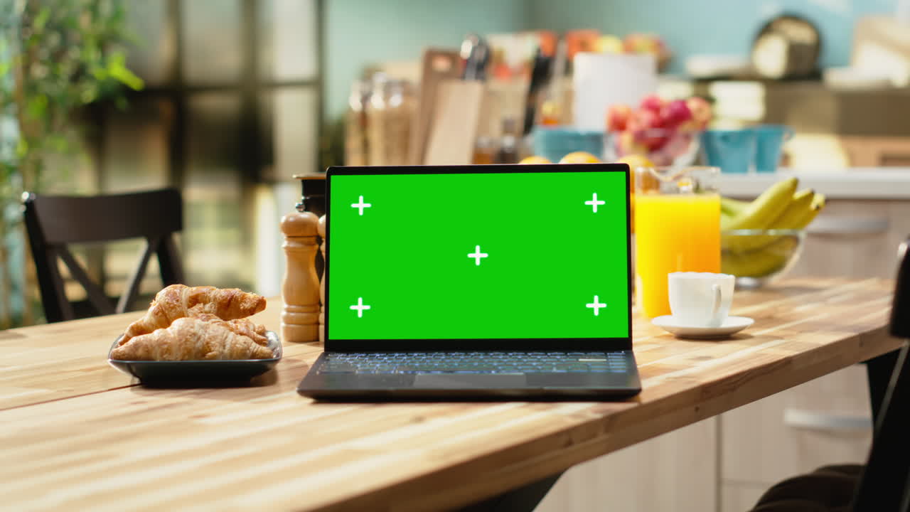 Laptop con schermo verde su tavolo di legno in cucina luminosa e vuota