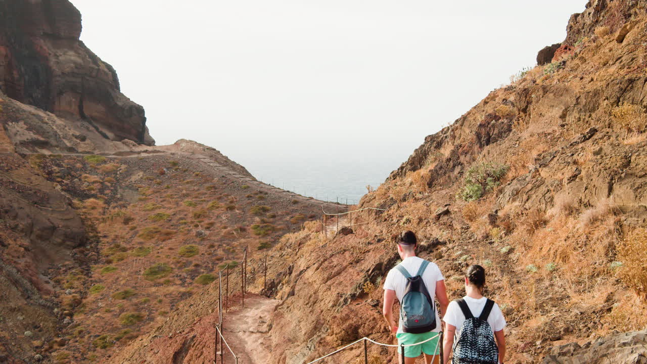Young Couple Walking On Narrow Trail At Ponta de Sao Lourenco In Madeira Island, Portugal. - wide