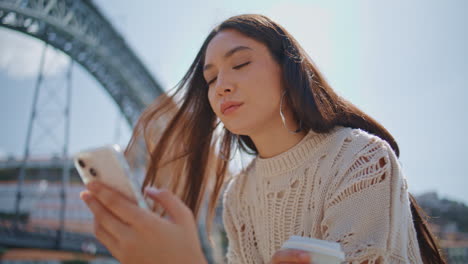 relaxed model texting mobile phone sms at sunshine closeup. girl holding coffee