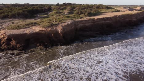 Luftaufnahme-Von-Menschen,-Die-Während-Des-Sonnenuntergangs-Auf-Den-Großen-Klippen-Von-Mar-Del-Plata-In-Argentinien-Spazieren-Gehen---Wellen,-Die-Gegen-Eine-Felswand-Schlagen