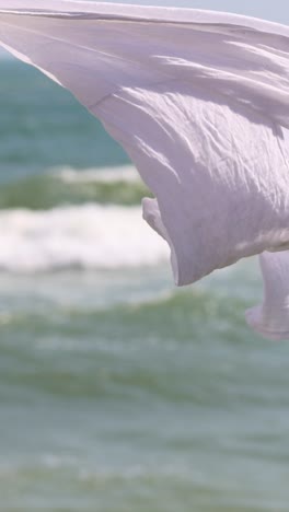 white cloth billows against a backdrop of ocean waves.