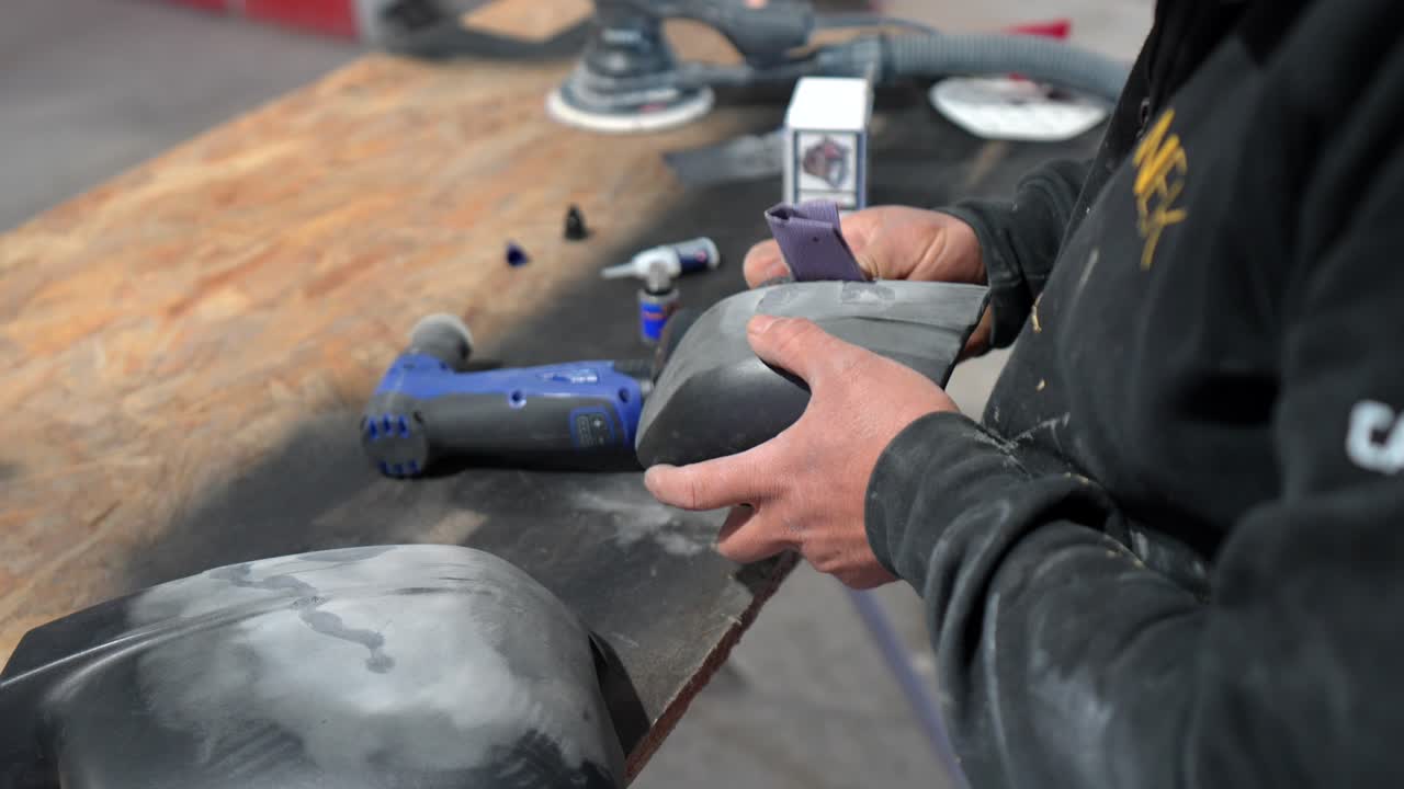 Worker's Hands Sanding a Car Part in an Automotive Workshop