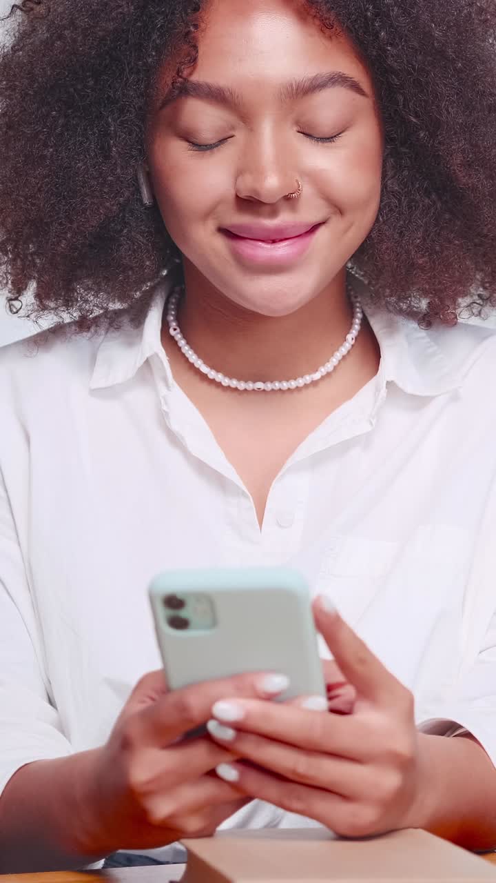 Giovane donna afroamericana allegra gioca con lo smartphone seduta al tavolo