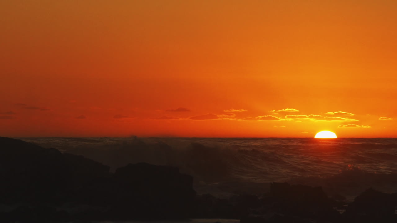 Goldener Sonnenuntergang über rauen Meereswellen, die Gischt erzeugen – Statische Aufnahme.