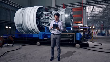 full body side view of an asian male professional worker with his tablet with airplane engine maintenance conducted, analytics checking the turbine, typing on his tablet's keybaord with meditation