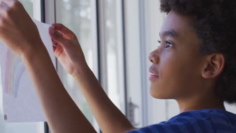 Boy-sticking-a-rainbow-painting-on-the-window-at-home