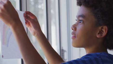 boy sticking a rainbow painting on the window at home