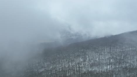 drone emerges from the fog over top of cloud covered mountain