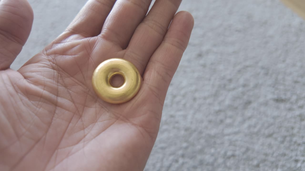 Close-up shot of a male's hand showcasing a rare doughnut-shaped 9999 fine gold cast bullion bar, highlighting its smooth texture and rich golden shine.