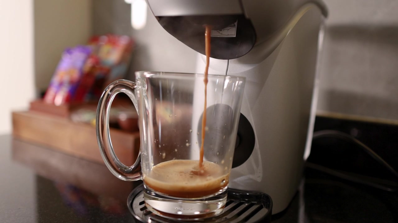 Café expresso quente sendo preparado por uma cafeteira automática em uma caneca de vidro transparente em ambiente interno