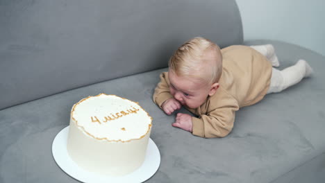 little baby boy lies on sofa on his belly. adorable child near the cake with a sign of four months.