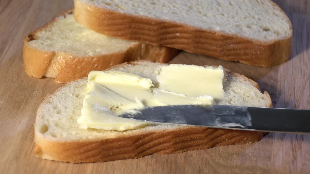 Un trozo de pan blanco con mantequilla gira sobre un fondo gris