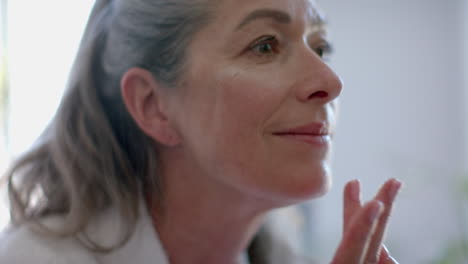 applying skincare, mature woman gently touching face, focusing on self-care routine