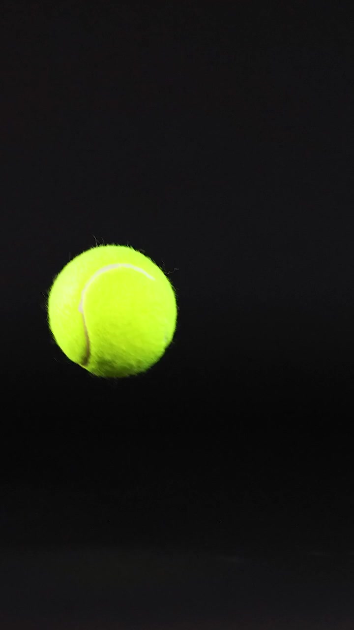 A tennis ball moves across a dark surface