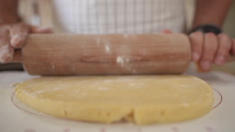 primer plano de un panadero desplegando masa de hojaldre hacia la cámara