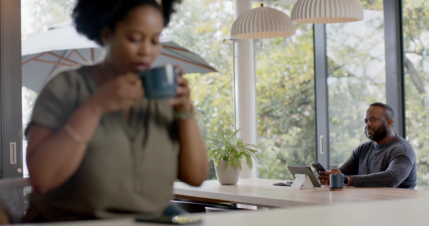 Coppia africana in cucina al mattino, la donna controlla il telefono e sorseggia da una tazza mentre l'uomo usa il tablet