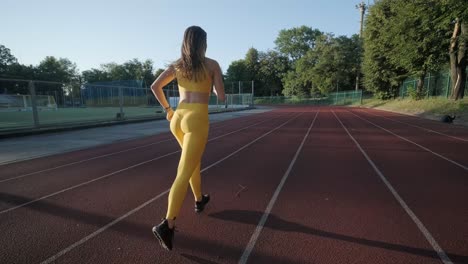 mujer corriendo en una pista al aire libre con ropa deportiva en un campo atlético