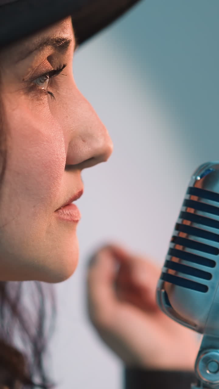 vista lateral cercana de un cantante con un sombrero negro y sosteniendo un micrófono vintage, el perfil facial y la expresión del cantante se destacan contra un fondo blanco a medida que la cámara se aleja
