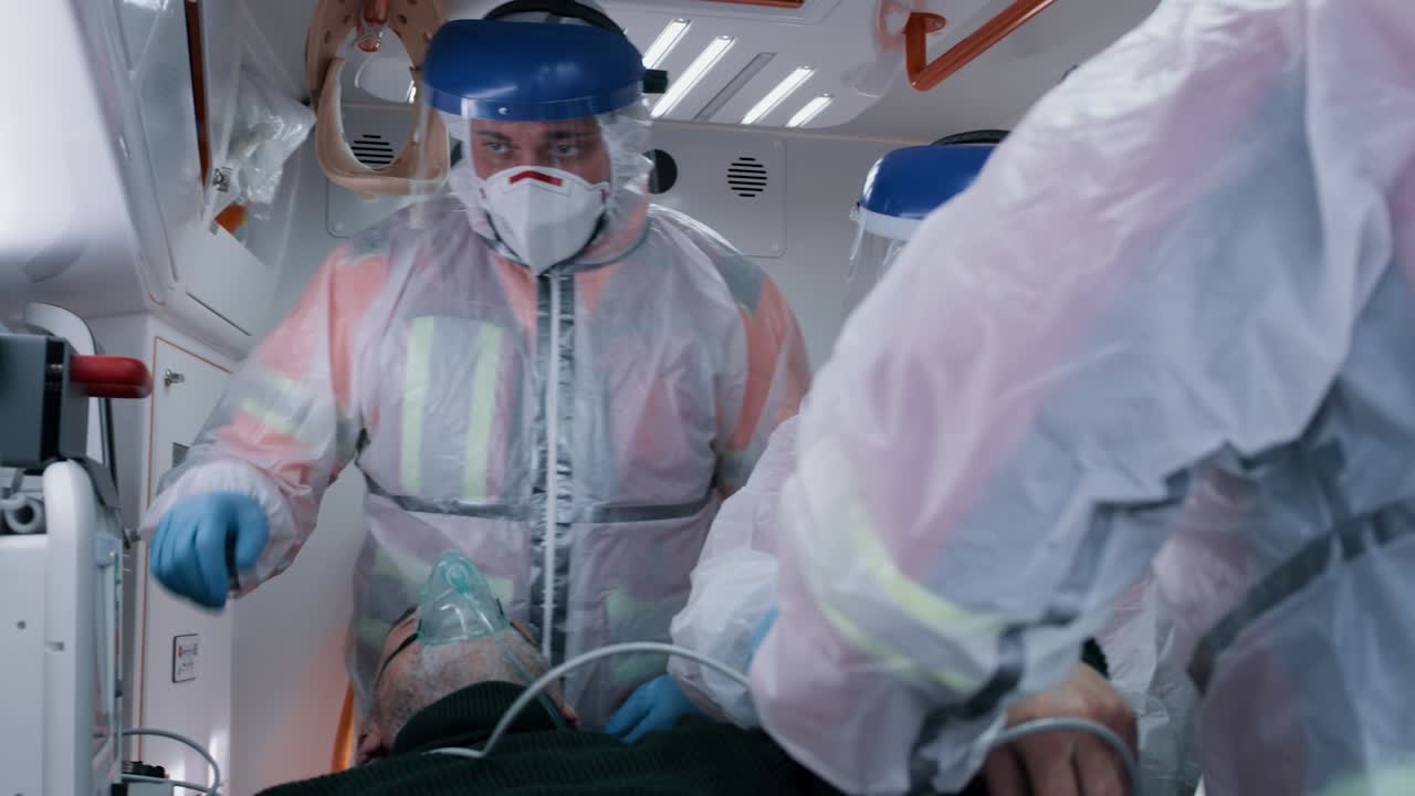 paramedics Measuring Blood Pressure of Patient Emergency Medicine Team in Hazmat Suits Putting Blood Pressure Cuff on Arm of Senior Man in Oxygen Mask while Working in Ambulance on Ride to Hospital