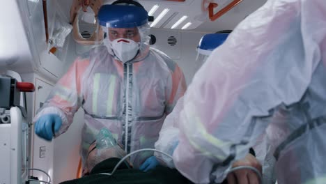 paramedics measuring blood pressure of patient emergency medicine team in hazmat suits putting blood pressure cuff on arm of senior man in oxygen mask while working in ambulance on ride to hospital