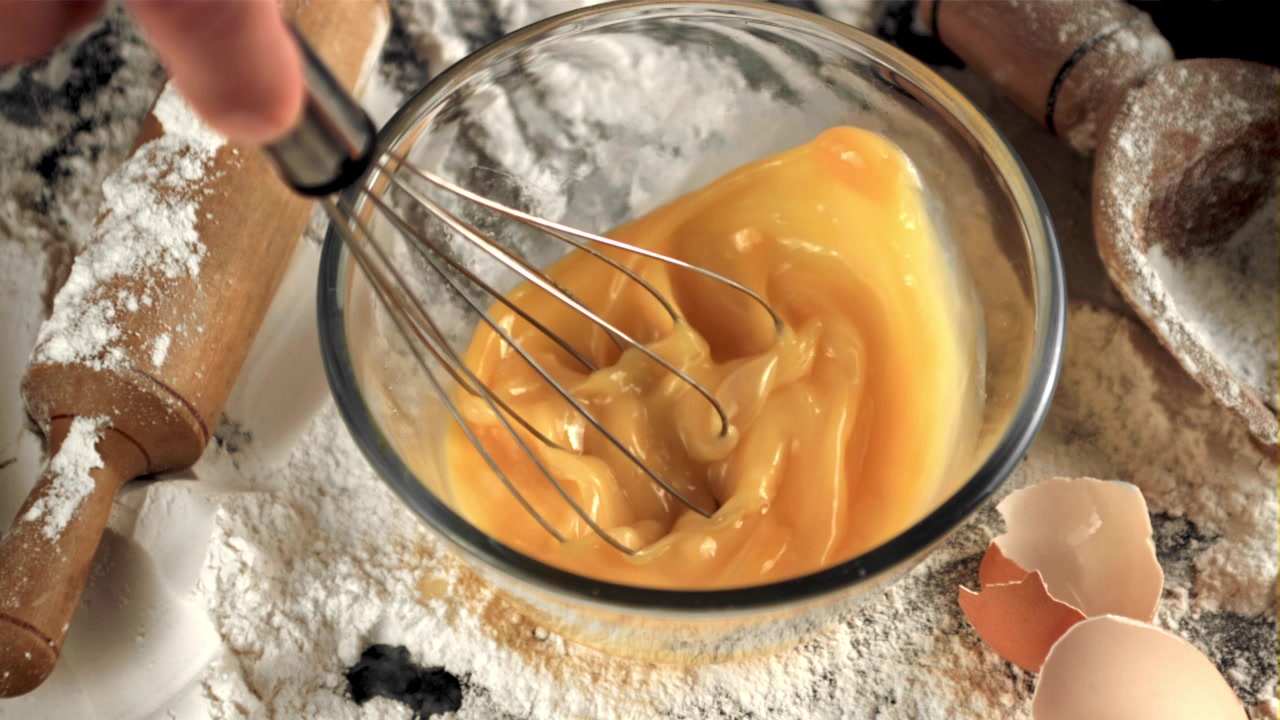 Close-up of Hand Whisking Eggs in a Glass Bowl for Baking