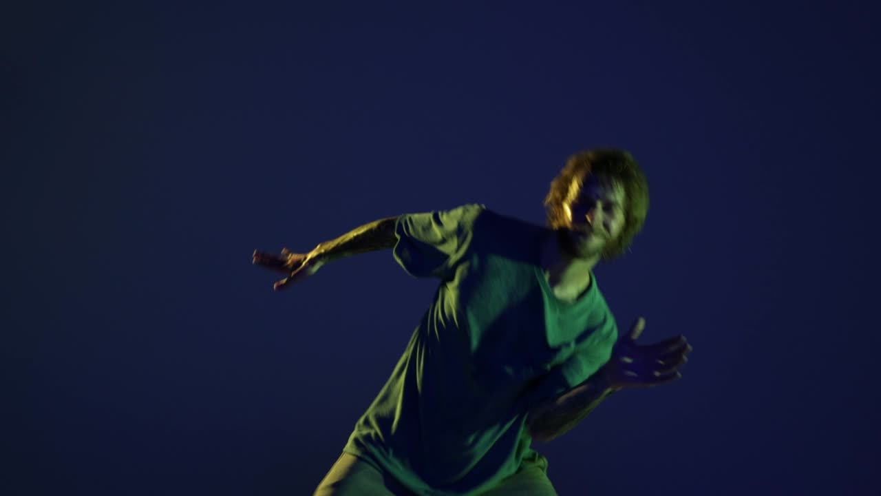 One happy young man, hip-hop dancer dancing isolated over dark blue background in neon light. Modern dance art, fashion, youth, ad, style. 4K, video