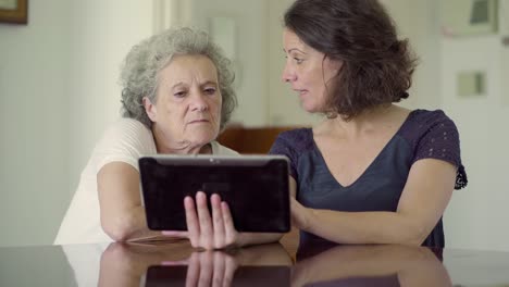 two women sitting at table and using tablet.