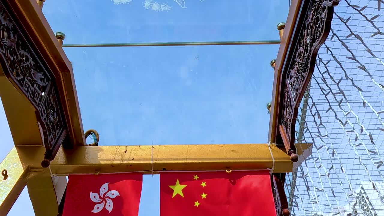 Close-up of Chinese and Hong Kong flags hanging beneath a decorative arch with a city skyline backdrop.